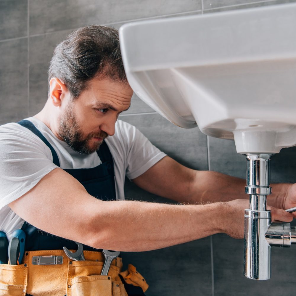 focused-male-plumber-in-working-overall-fixing-sink-in-bathroom.jpg